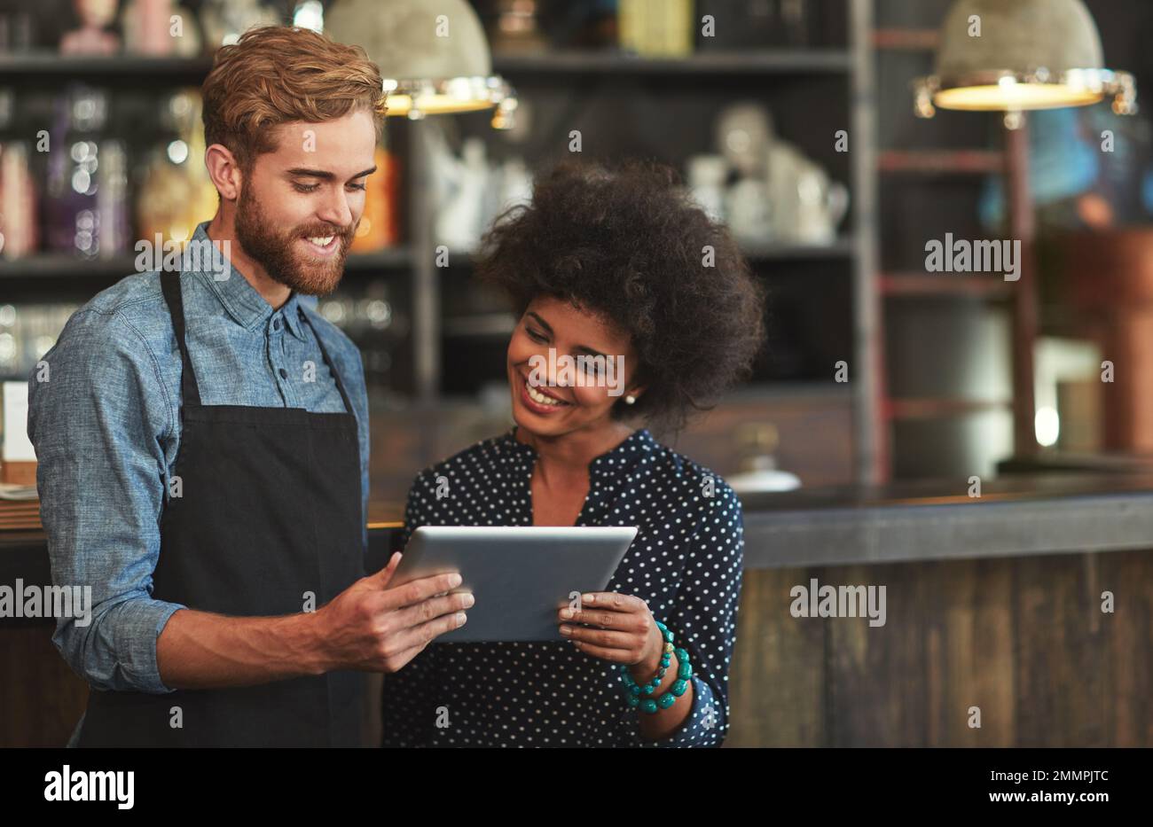 Leggere i commenti sul loro sito web caffè. i giovani dipendenti di una caffetteria che utilizzano un tablet digitale insieme. Foto Stock