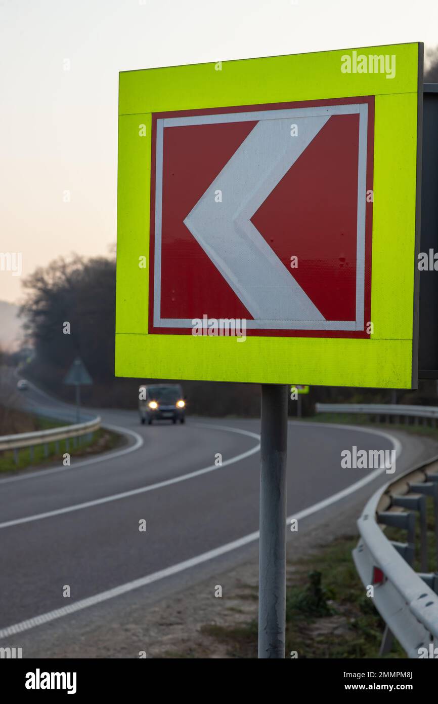 Strada asfaltata con segnaletica stradale brillante in loco della curva a sinistra. Foto Stock
