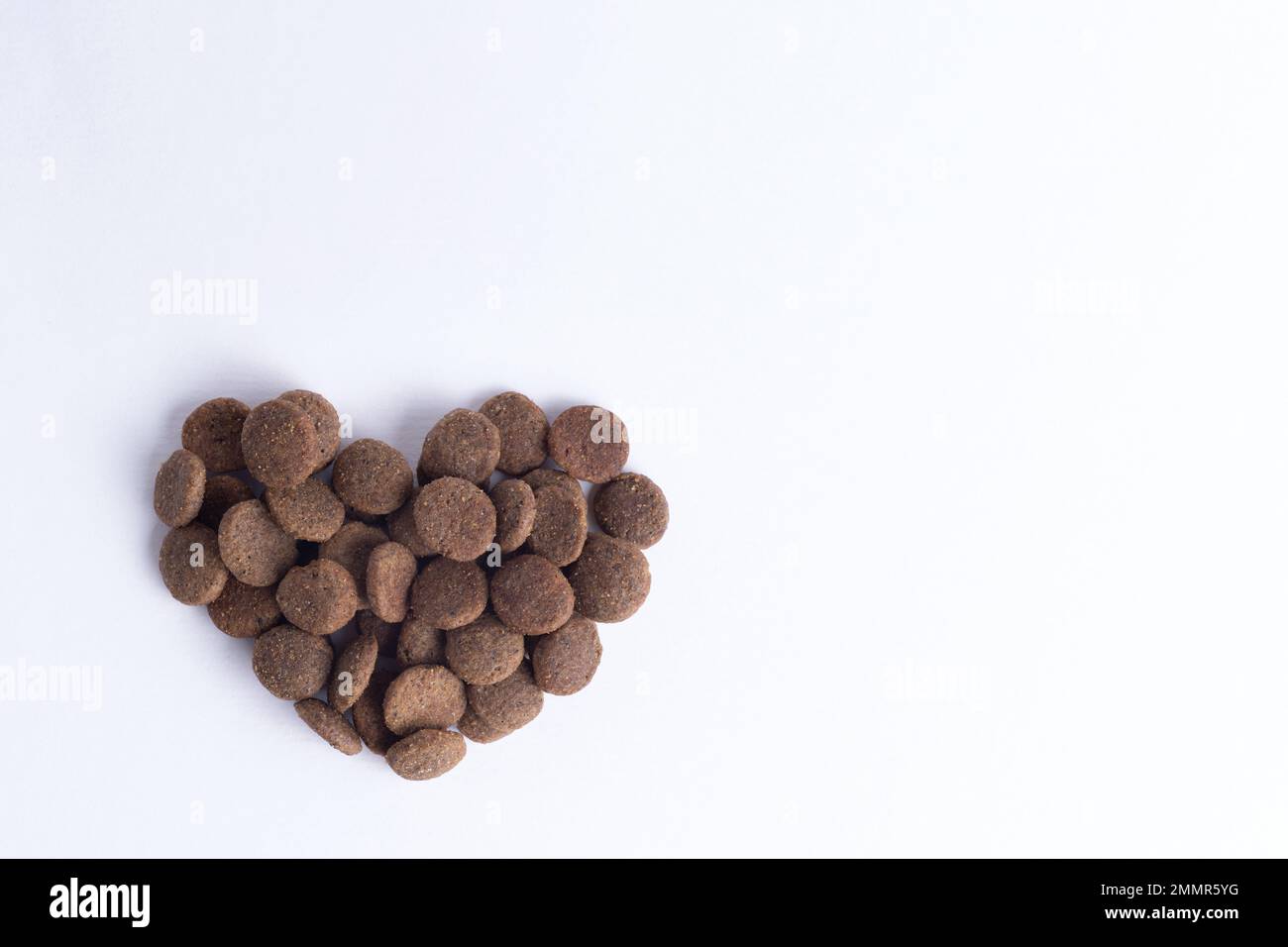 Cibo secco per cani e gatti a forma di cuore isolato su sfondo bianco, spazio copia, vista dall'alto. Il concetto di amore per gli animali domestici. Animale sano f Foto Stock