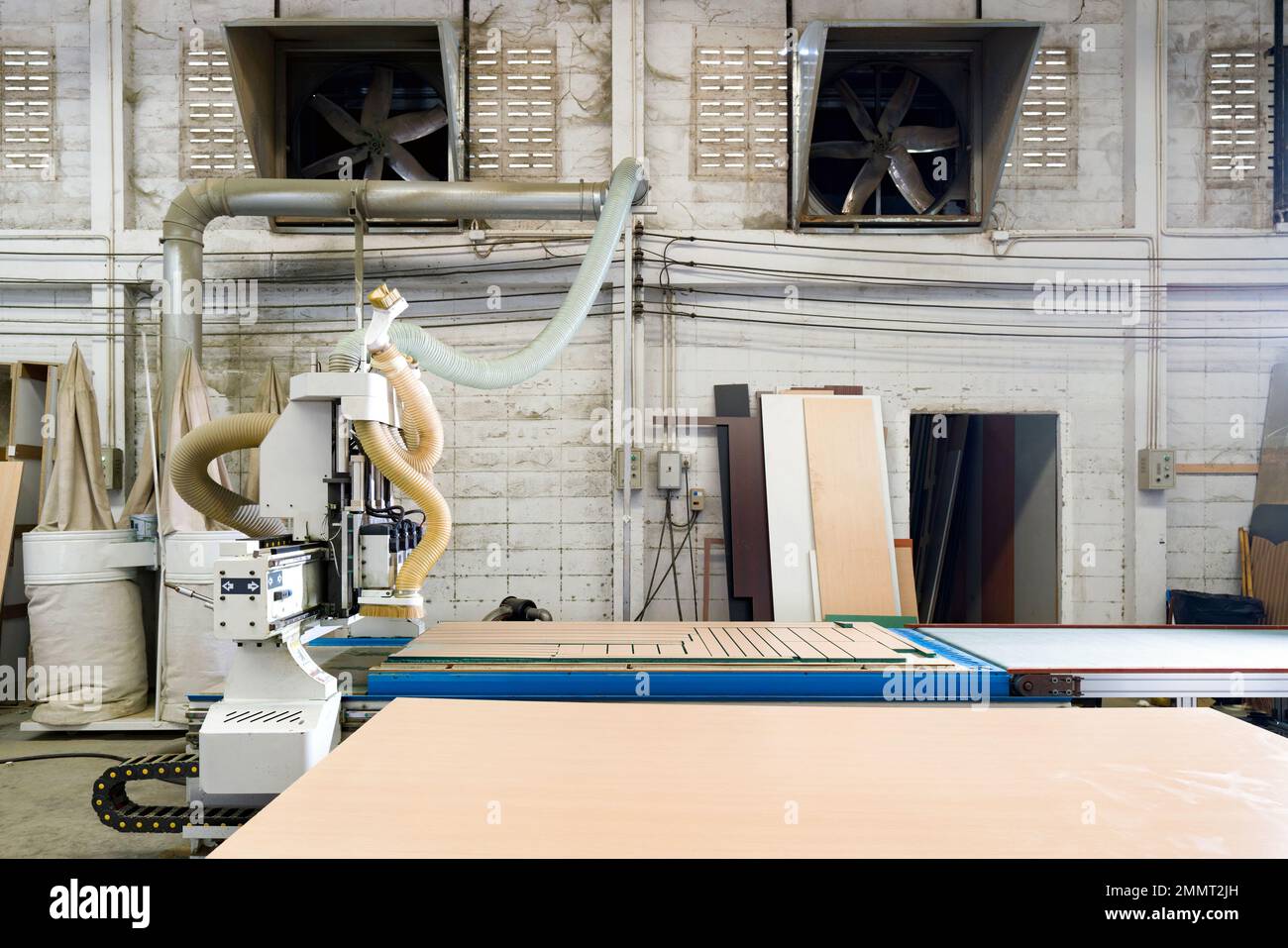 Piano di lavoro completamente caricato con legno compensato in fabbrica industriale che produce parti di mobili in legno. I ventilatori di scarico sono su una parete di mattoni in cemento leggero Foto Stock