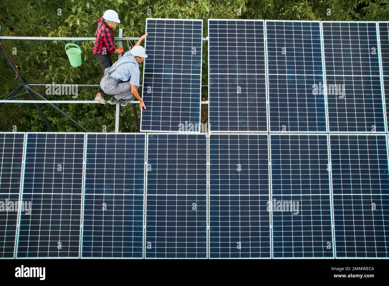 Due uomini in caschi di sicurezza che installano pannelli solari fotovoltaici. Tecnici maschili che collocano il modulo solare sulla struttura di supporto durante l'assemblaggio del sistema di pannelli fotovoltaici solari. Foto Stock