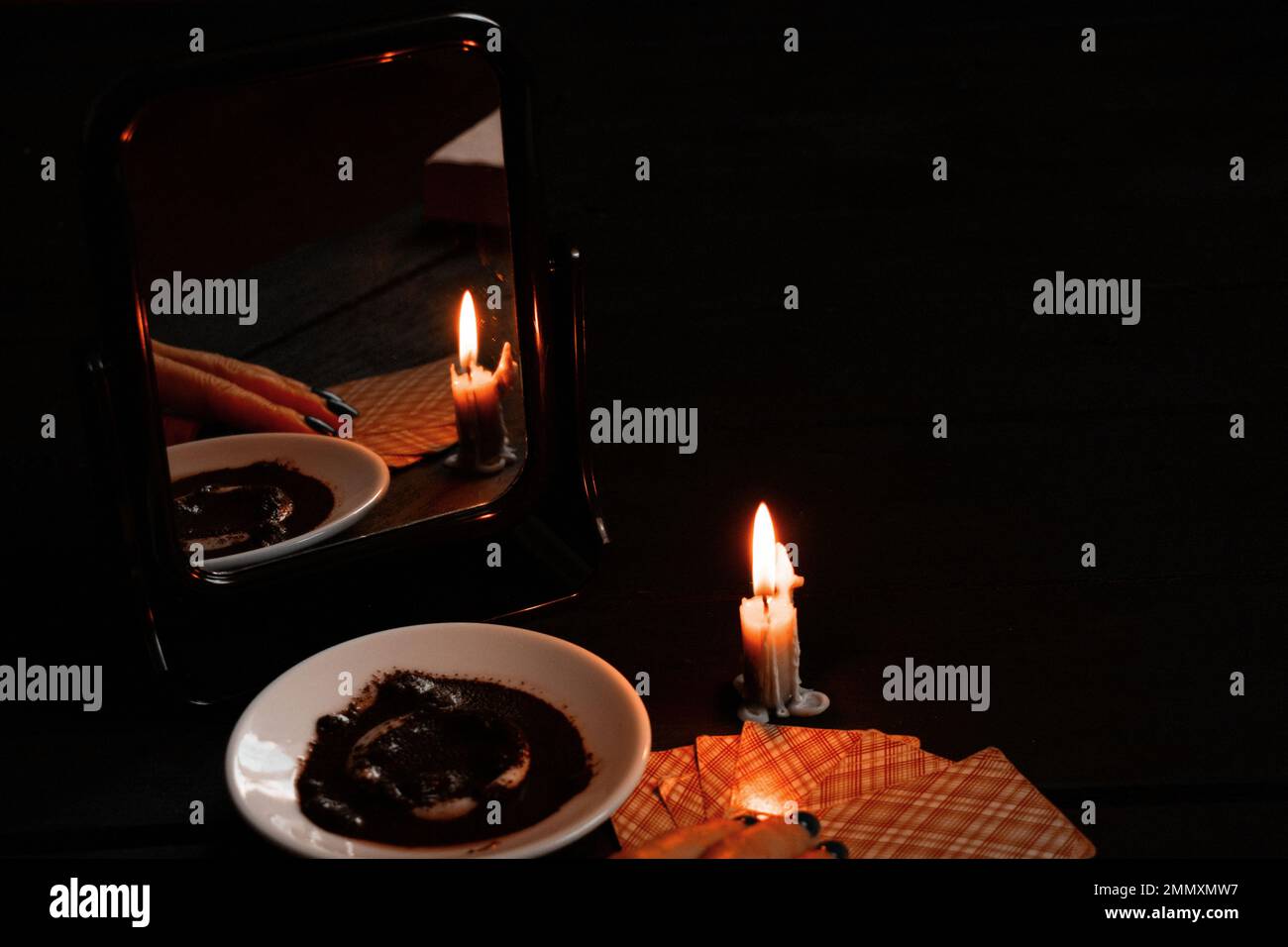 una candela che brucia è stata portata dagli specchi e ci sono carte che raccontano la fortuna e le basi del caffè in un piatto vicino, fortuna che dice sulle carte da candele Foto Stock