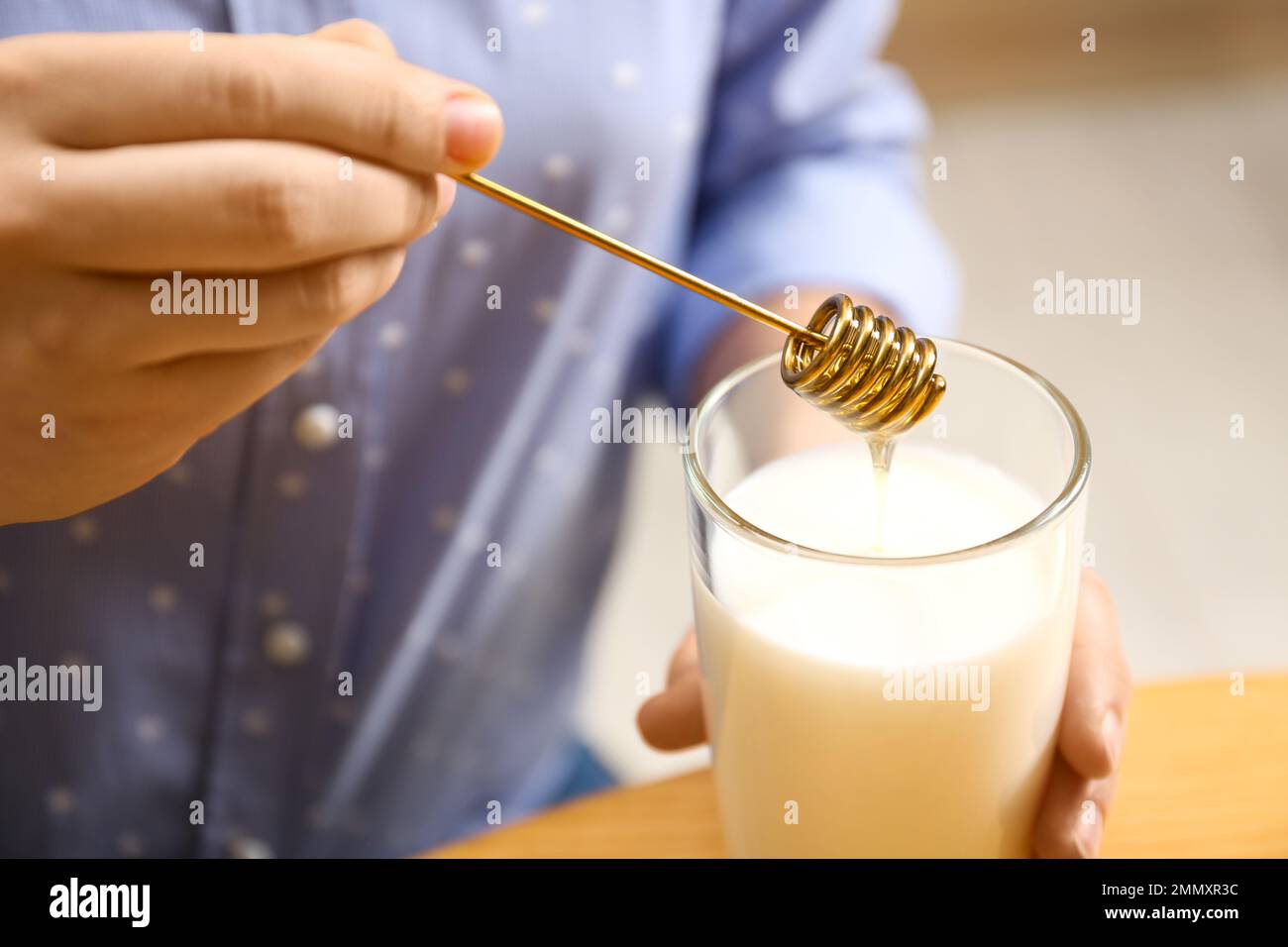 Donna che aggiunge miele al latte a tavola, primo piano Foto Stock