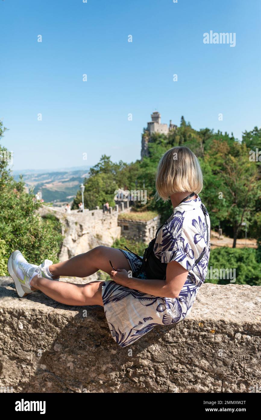 Giovane bella donna siede e sorride sullo sfondo della Fortezza di Guaita nella Repubblica di San Marino sul Monte Titano, Italia Foto Stock