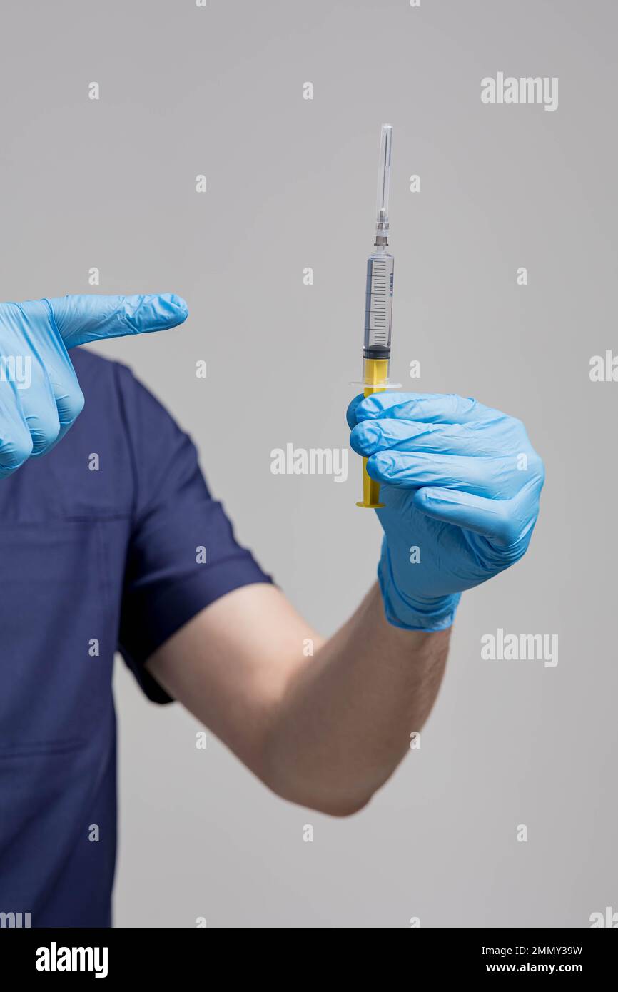 Chiudere la mano del medico in un guanto di gomma che contiene una siringa trasparente senza cappuccio con vaccino su sfondo chiaro. Concetto di rifiuto delle vaccinazioni Foto Stock