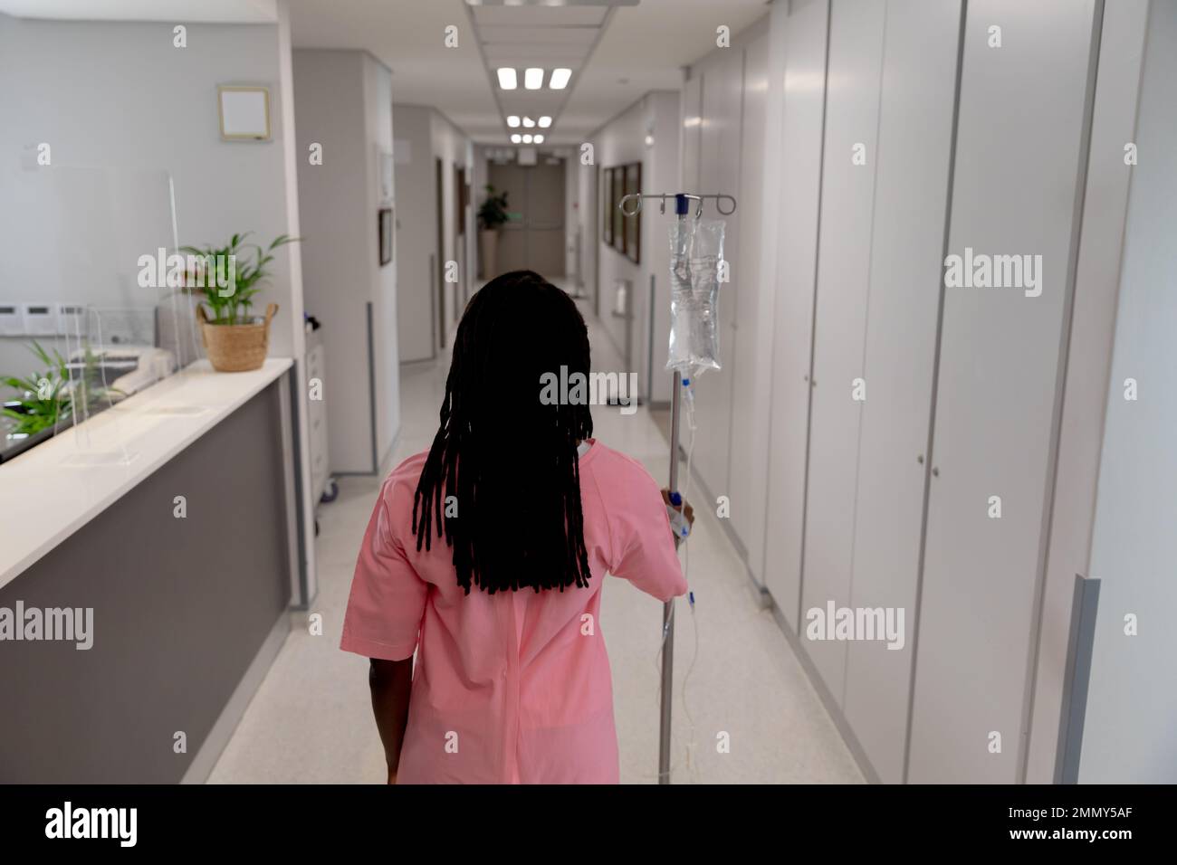 Paziente femmina afro-americana che cammina attraverso corridoio con gocciolamento all'ospedale Foto Stock