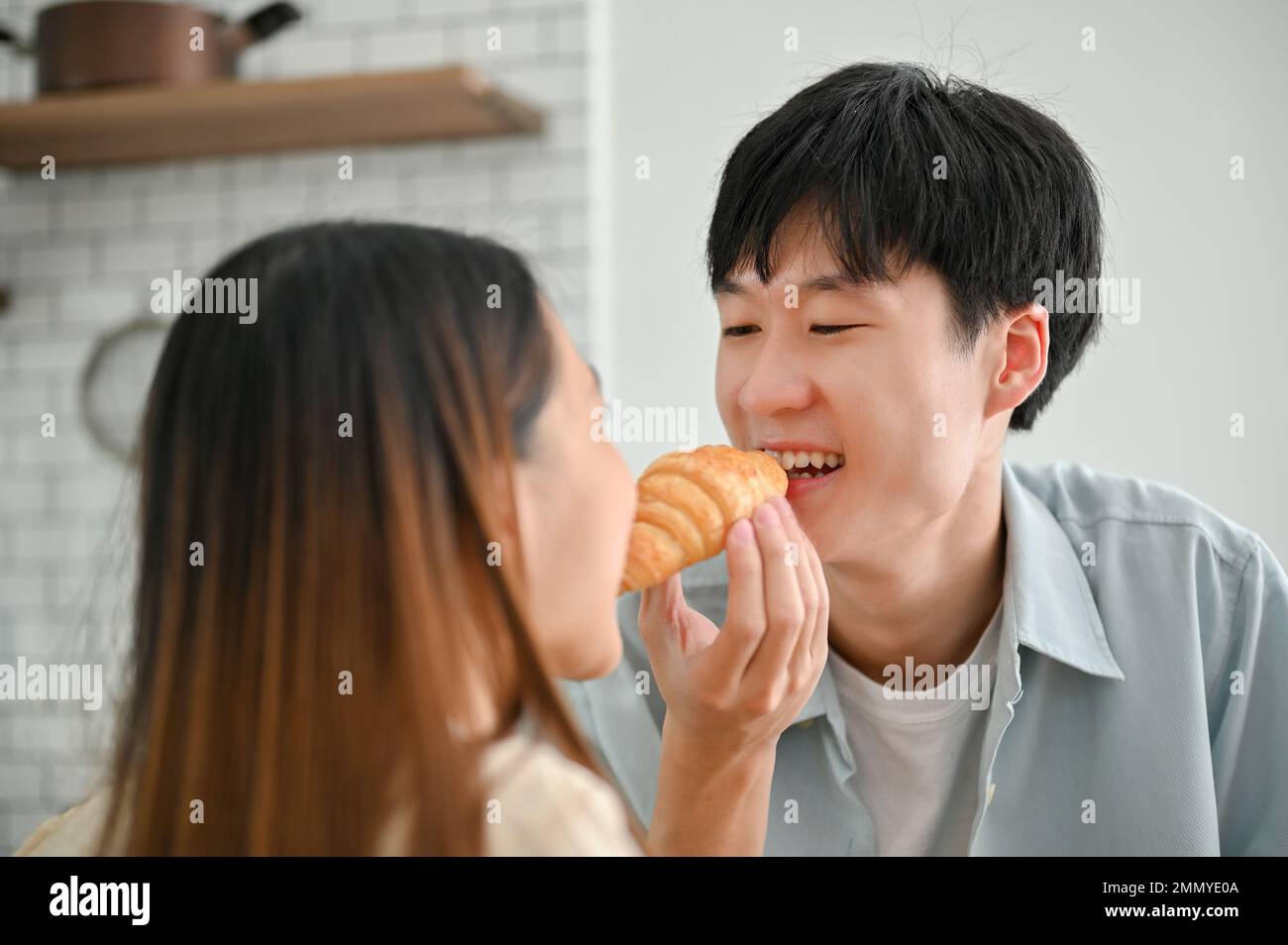 Coppia asiatica che ama mangiare insieme croissant in cucina, fare colazione insieme, mostrando amore e cura. nel concetto di coppia di amore Foto Stock