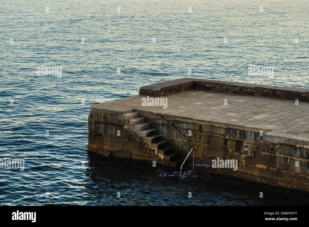 Scale in cemento e molo in pietra nella città di Lovran, nel golfo del Quarnero del mare Adriatico al tramonto Foto Stock