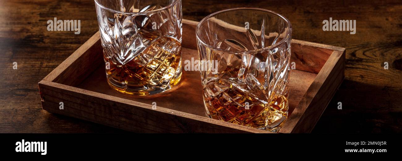 Whiskey in bicchieri con panorama sul ghiaccio. Whisky borbonico sulle rocce su sfondo scuro, banner panoramico Foto Stock