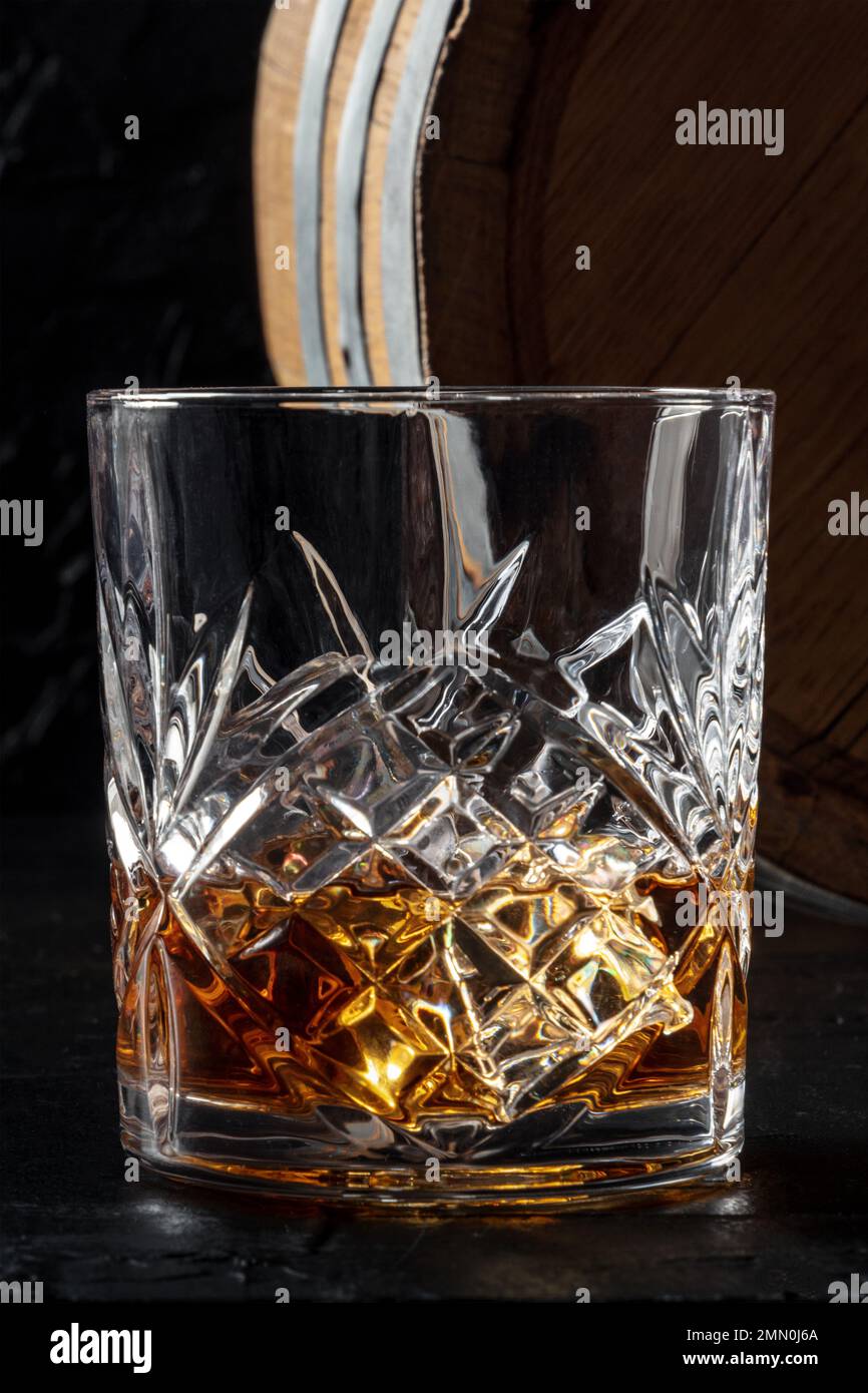 Frullare in un bicchiere con un barile. Whisky borbonico e una botte su sfondo scuro, un primo piano della classica bevanda di lusso Foto Stock