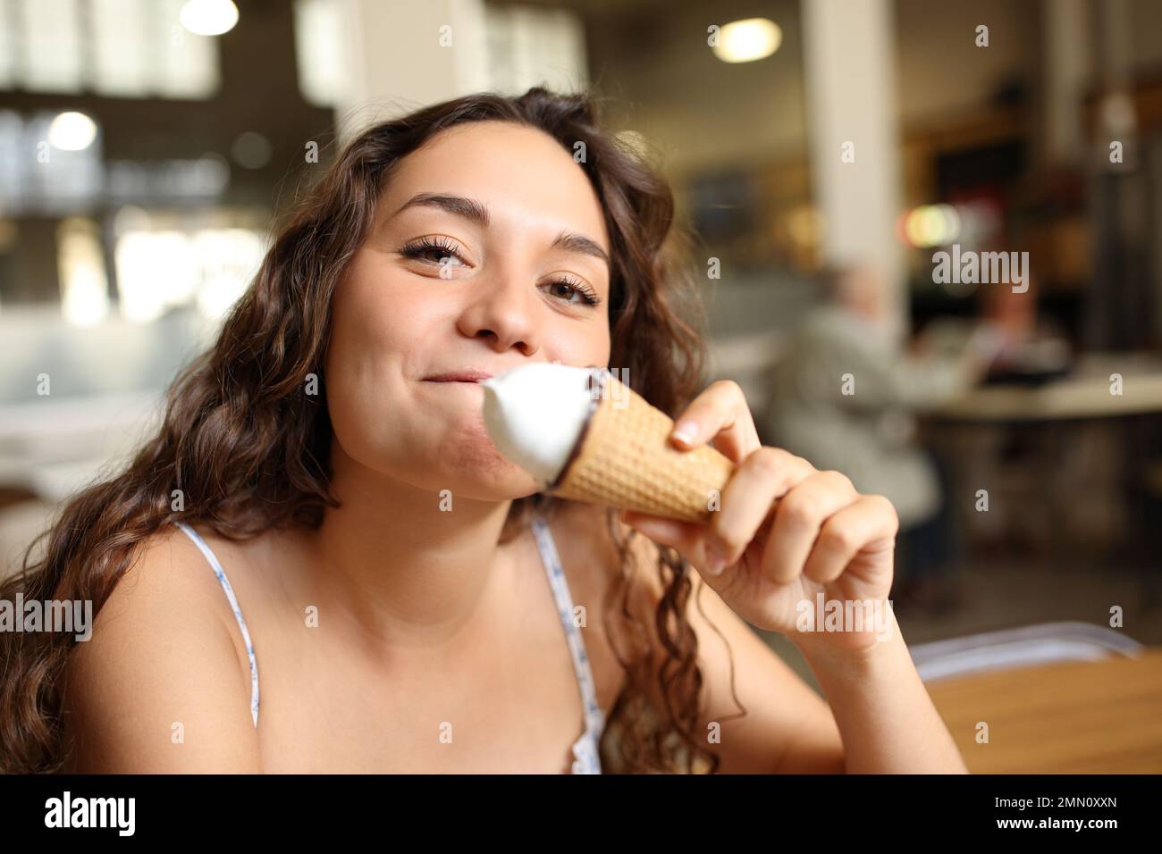 Una donna felice che mangia gelato ti guarda in un bar Foto Stock