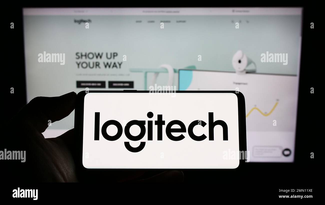 Persona che tiene uno smartphone con il logo della società svizzera Logitech International S.A. sullo schermo di fronte al sito Web. Messa a fuoco sul display del telefono. Foto Stock