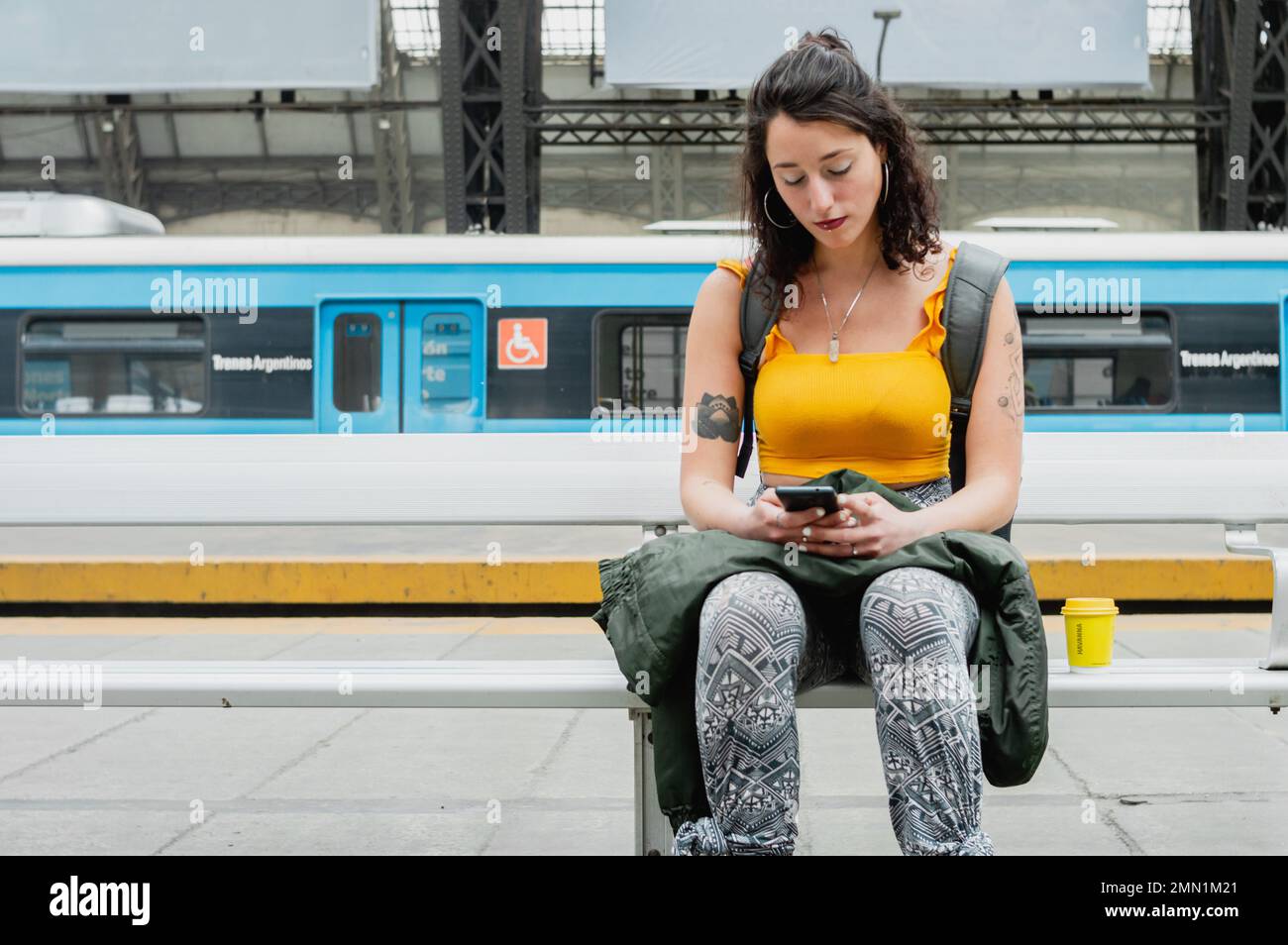 giovane donna latina di etnia argentina, seduta tranquilla alla stazione ferroviaria che controlla l'orario di imbarco sul telefono, concetto di viaggio, spazio copia. Foto Stock
