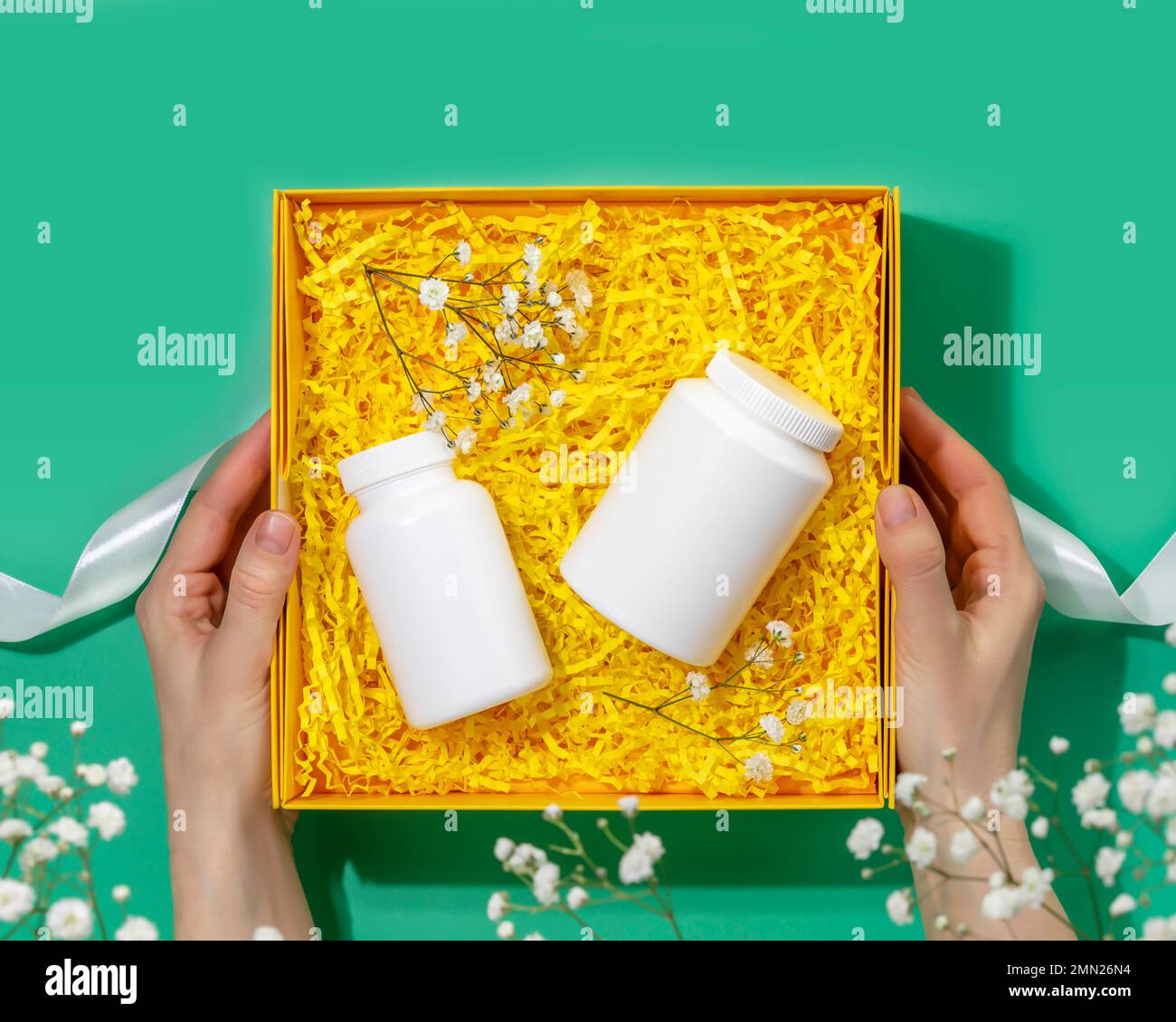 Le mani femminili tengono la scatola del regalo con le vitamine naturali ed i supplementi insieme. Preparazione pacchetto salute, confezione regalo artigianato con bottiglie bianche farmacia. Beffa di Foto Stock