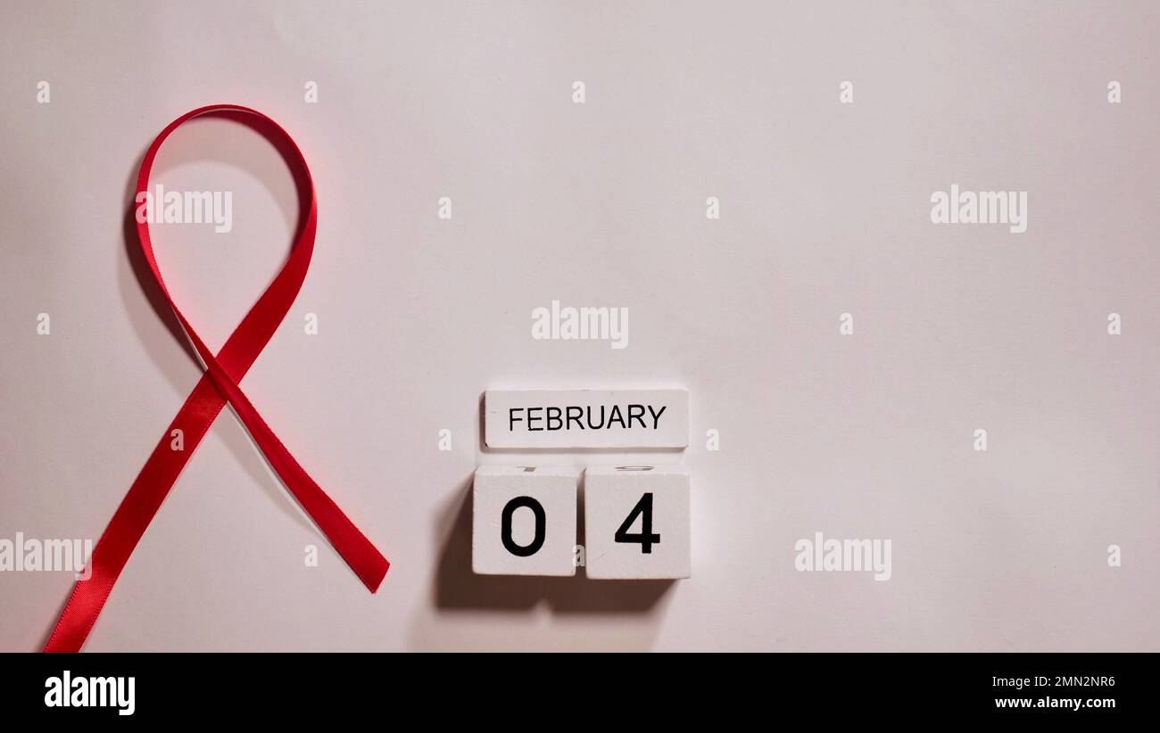 Simbolo della malattia del cancro con nastro rosso su sfondo bianco primo piano sul World Cancer Awareness Day 4 febbraio Foto Stock