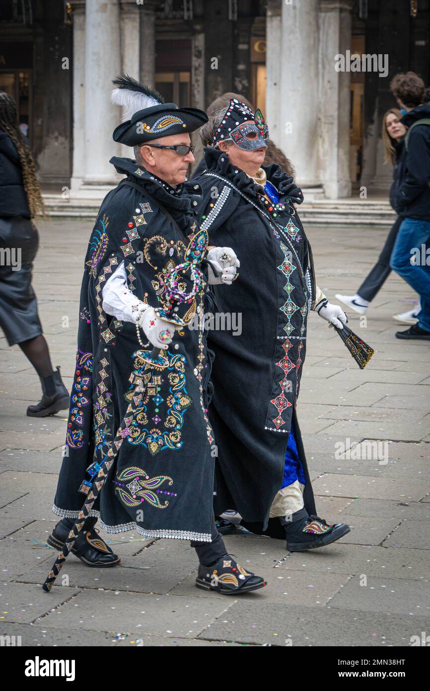 Una coppia anziana vestita di mantelli di carnevale ricamati neri cammina per la strada durante il carnevale veneziano Foto Stock
