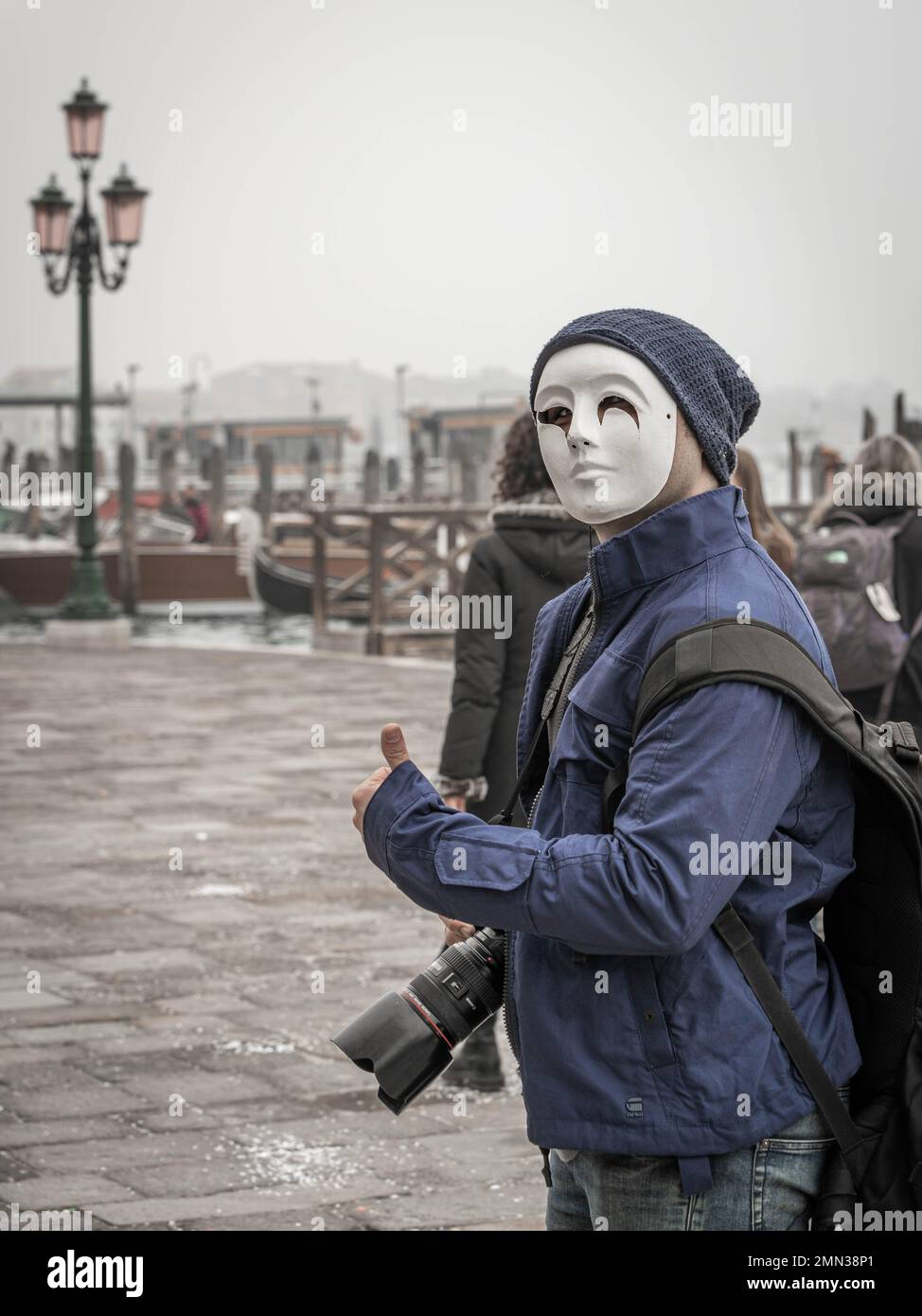 Un fotografo con una fotocamera professionale in maschera con lampione veneziano sullo sfondo di Piazza San Marco durante il Carnevale tradizionale. Foto Stock