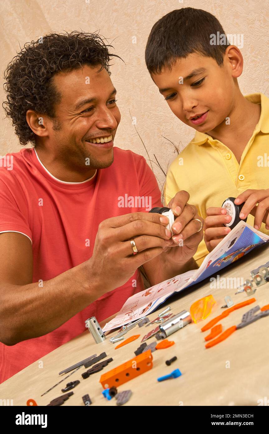 Giovane ragazzo e un maschio adulto controllano le istruzioni e assemblano insieme un kit auto giocattolo in metallo e plastica Foto Stock
