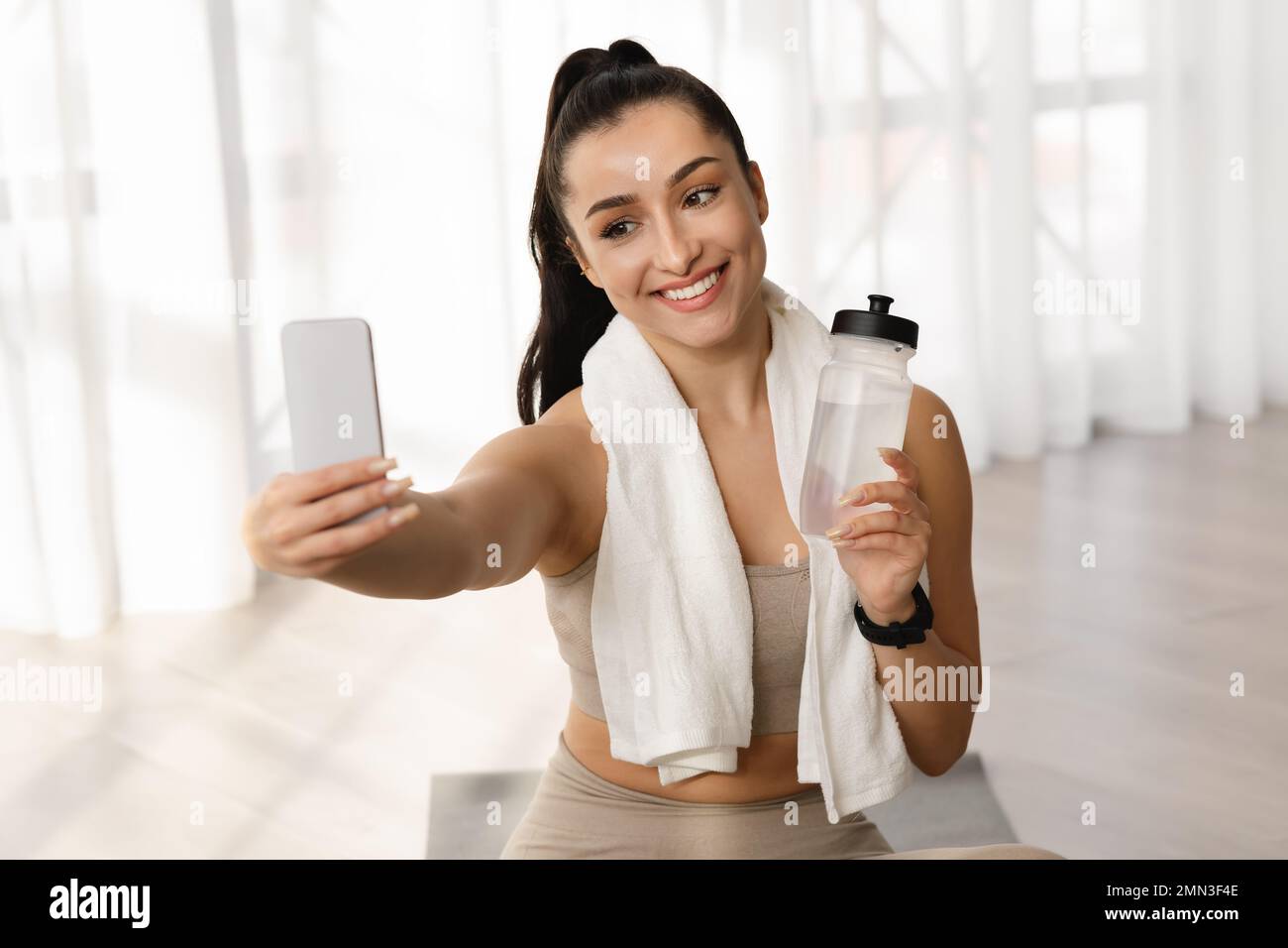 Bella donna fitness blogger prendere selfie, mostrando bottiglia di acqua Foto Stock