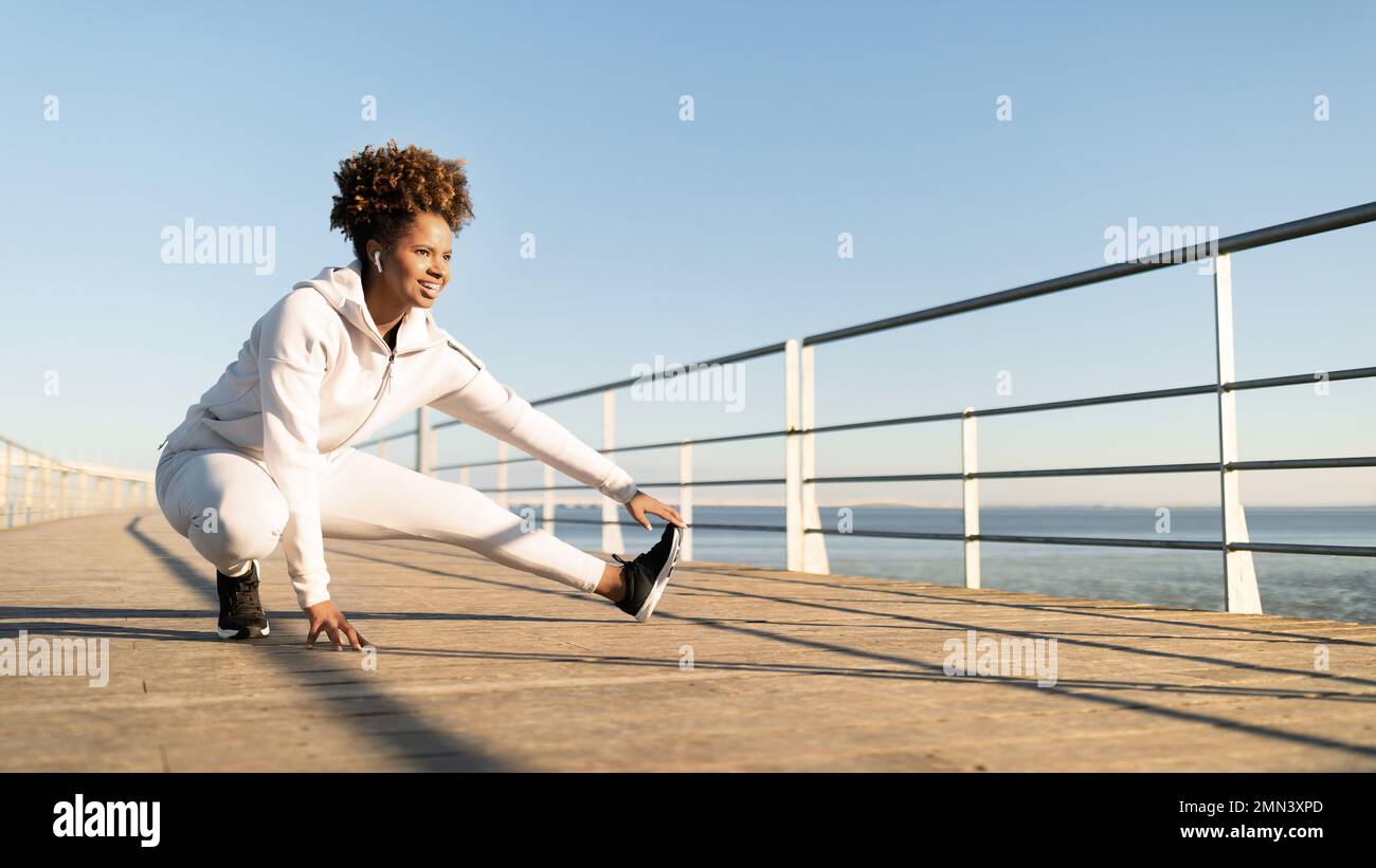 Sporty Black Female Stretching gambe muscoli, scaldarsi mentre allenarsi all'aperto Foto Stock