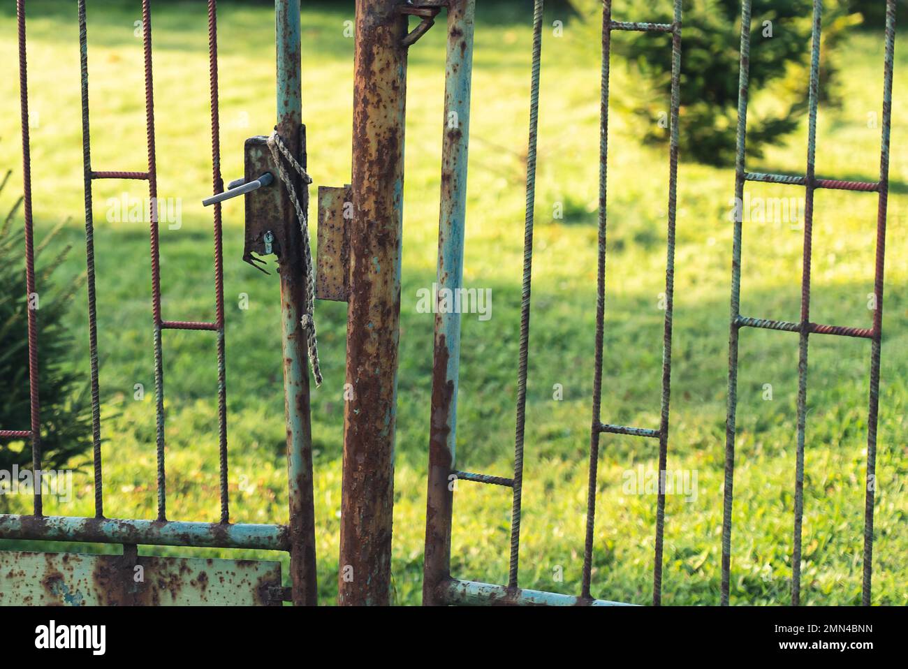 un vecchio, arrugginito cancello chiuso, che conduce ad un bel cortile pieno di erba e alberi. Foto di alta qualità Foto Stock