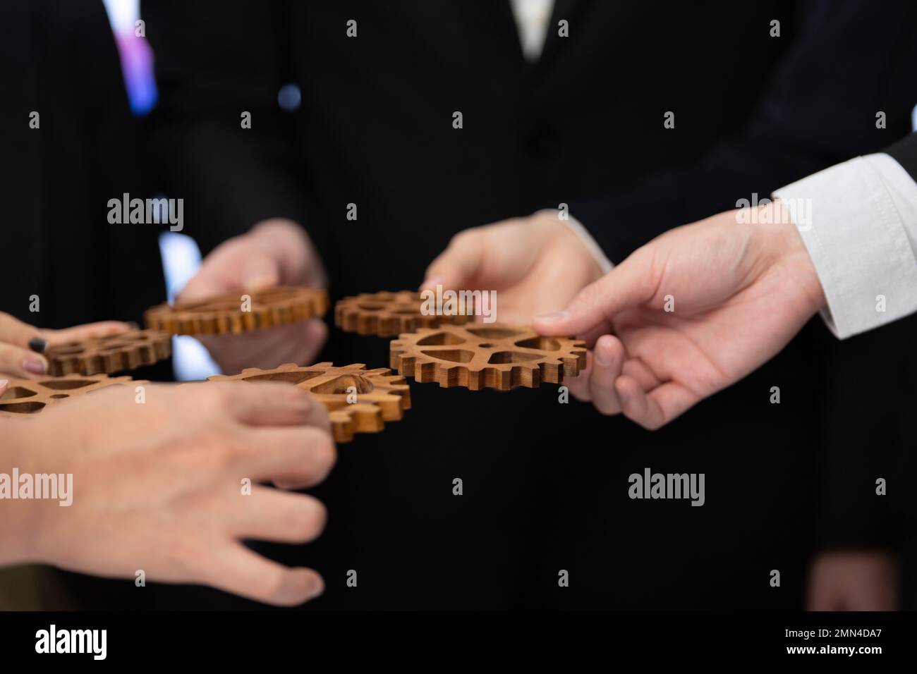 Closeup mano che tiene l'ingranaggio di legno da businesspeople vestito per sinergia di armonia nel concetto del posto di lavoro dell'ufficio. Gruppo di persone che fanno mano catena di Foto Stock