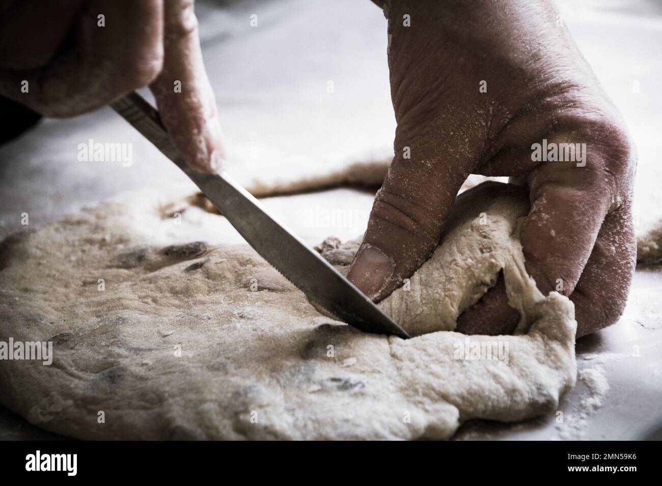 Le mani della nonna della donna che tagliano la pasta del pane su una superficie infarinata Foto Stock