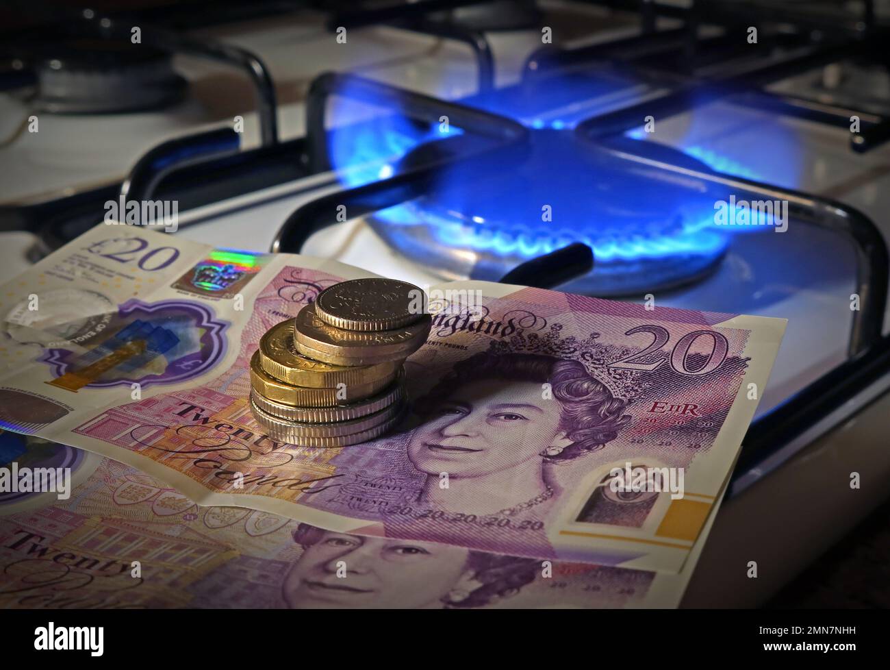 Possiamo permetterci di cucinare con il costo del gas nel 2023? Monete/banconote in sterline inglesi accanto a una fiamma a gas su un piano cottura da cucina Foto Stock
