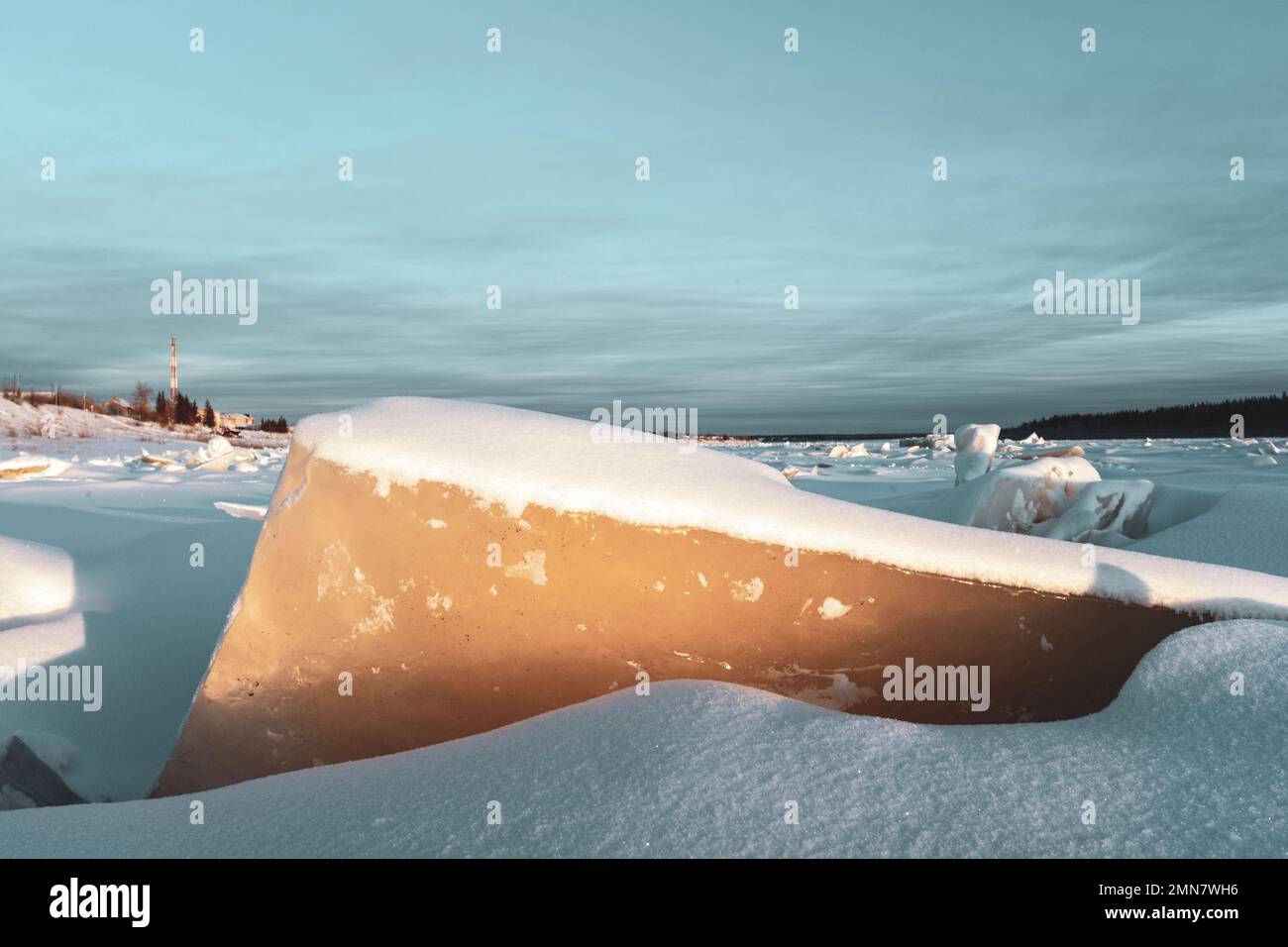 Un pezzo di ghiaccio si stacca dalla neve sul fiume ad un tramonto luminoso Vilyui in Yakutia sullo sfondo della torre della radio nel villaggio di sunt Foto Stock