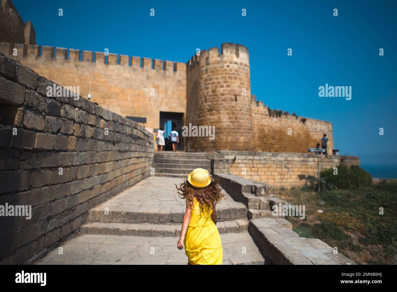 Una ragazza turistica in un cappello giallo e una sundress cammina lungo la strada della città vecchia fatta di pietra con una fortezza. Tour panoramico. Il bambino si è perso Foto Stock