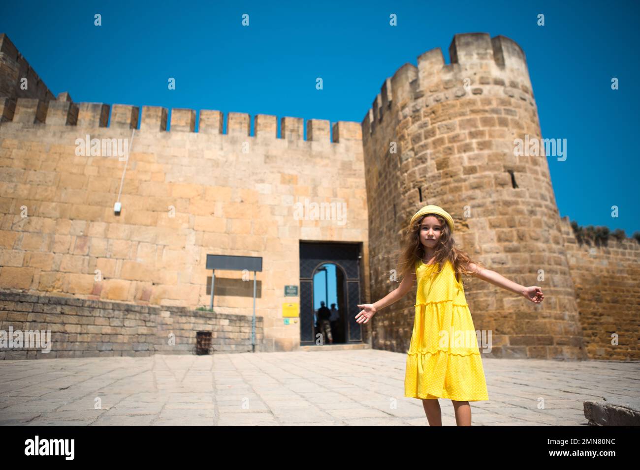 Una ragazza turistica in un cappello giallo e una sundress cammina lungo la strada della città vecchia fatta di pietra con una fortezza. Tour panoramico. Il bambino si è perso Foto Stock