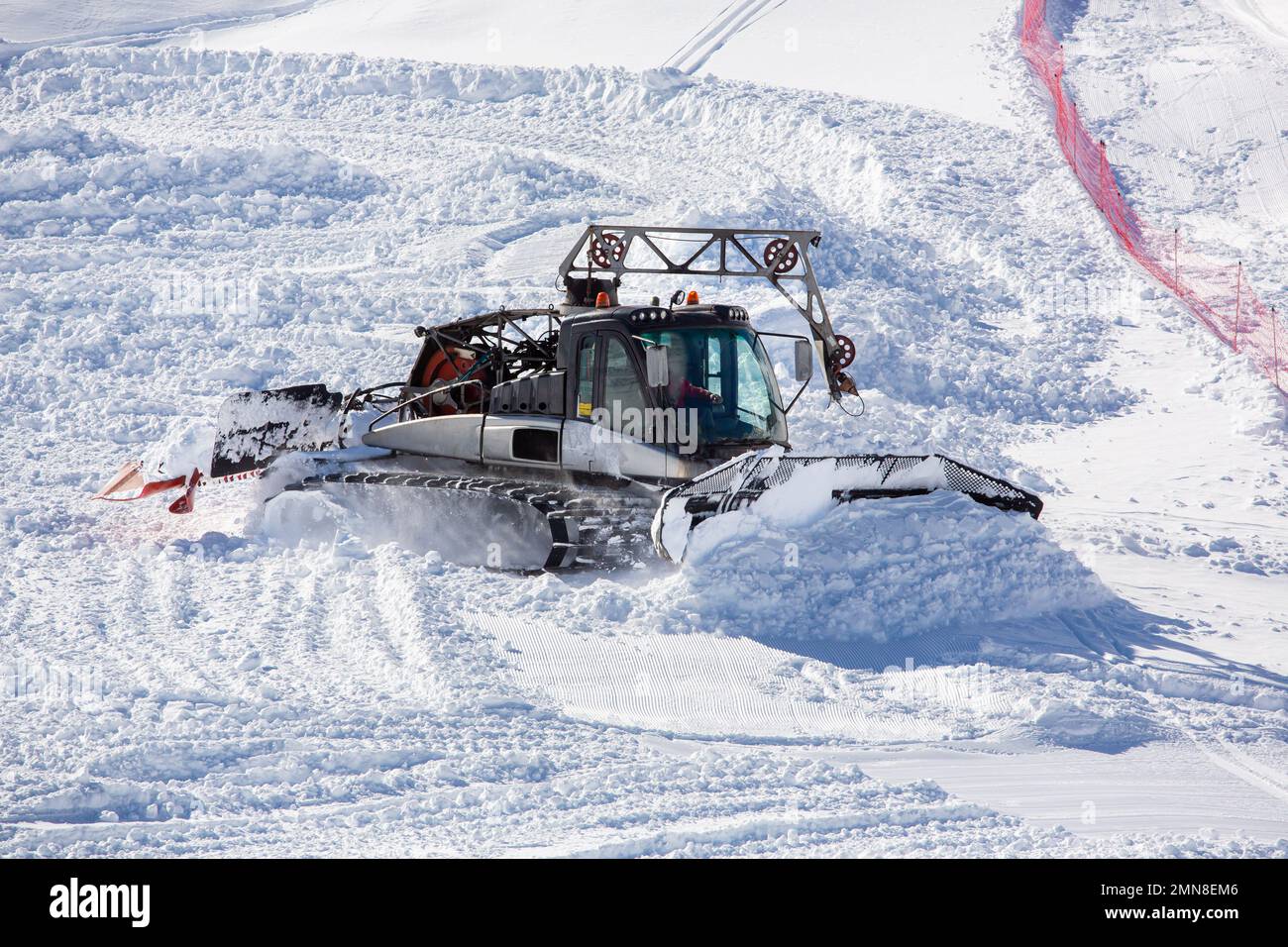 Uno spazzaneve in azione spazzando la neve in montagna. Un uomo al lavoro che guida uno spazzaneve in montagna. Lavorare in montagna con la neve Foto Stock