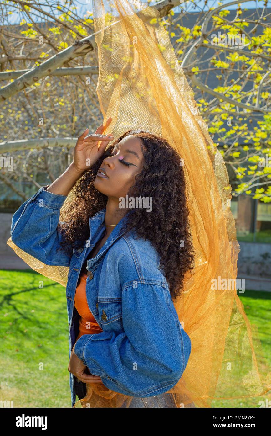 modello nero afro-americano di fronte alla giacca arancione tulle blu jean editoriale moda bellezza trucco farfalla cacoon posa urbana Foto Stock