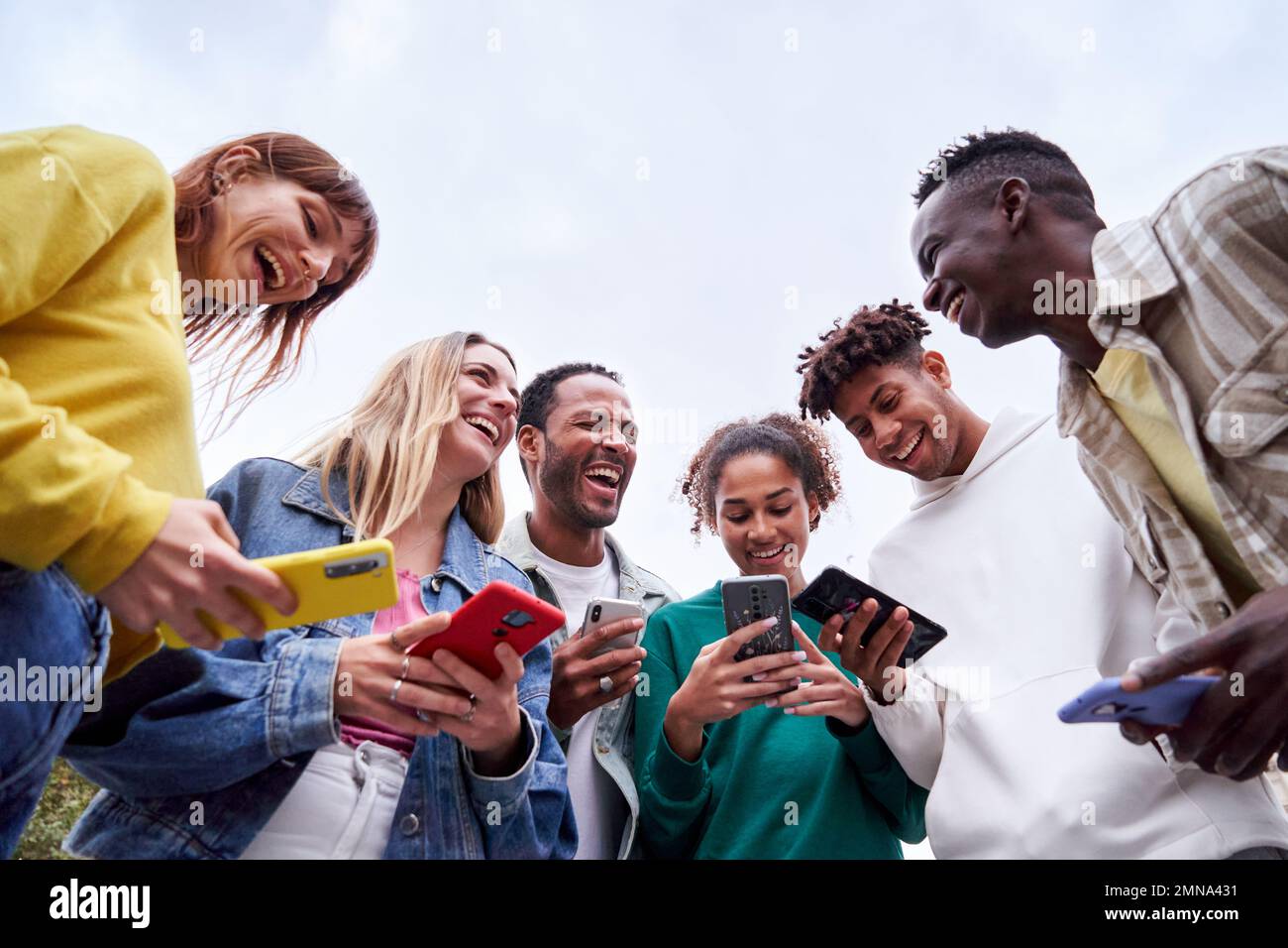 Studenti Erasmus multirazziali, in piedi all'aperto utilizzando i loro telefoni e ridendo insieme. Foto Stock
