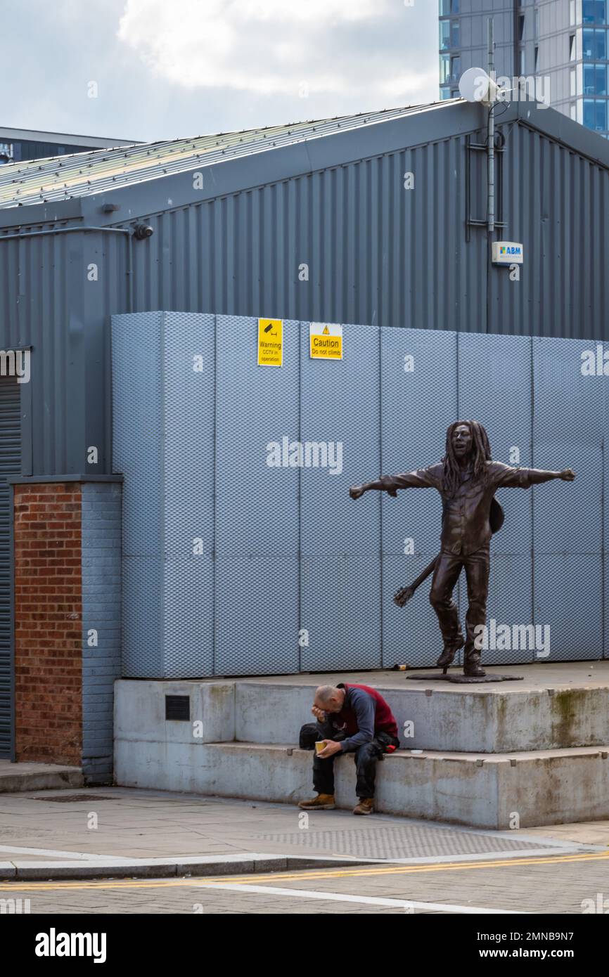 Uomo seduto di fronte alla statua di scultura di Happy Bob Marley a Liverpool, Regno Unito Foto Stock