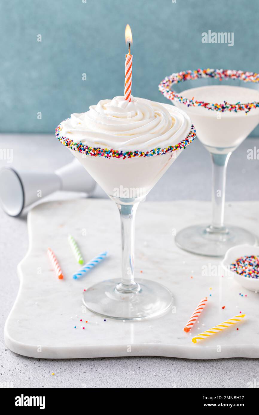 Torta di compleanno martini con spolverini sul bordo di vetro sormontato da panna montata con candela di compleanno Foto Stock