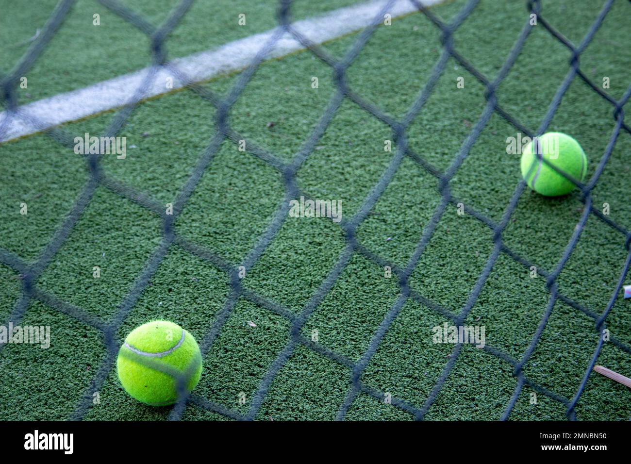 palle da tennis su un campo da paddle in erba artificiale visto dietro una recinzione Foto Stock