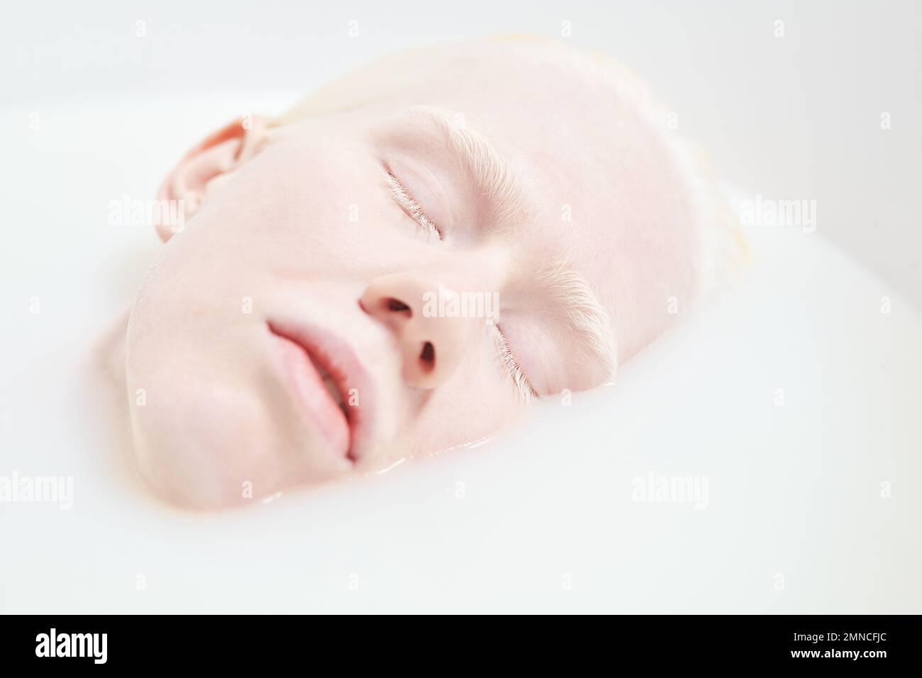 Primo piano di faccia pallida di giovane donna albina tranquilla o addormentata sdraiata nella vasca da bagno riempita con acqua calda e latte durante la procedura di bellezza Foto Stock