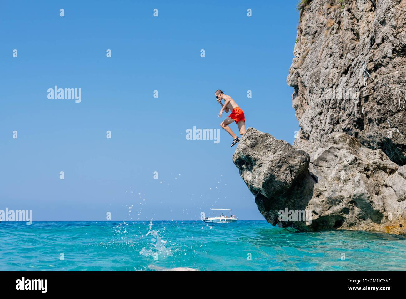 Il ragazzo adolescente salta da una roccia nel mare. Foto Stock