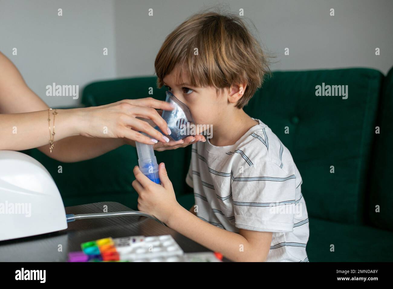 Donna che inala il bambino a casa con l'inalatore. Il ragazzino malato si siede sul divano. Vapori respiratori, malattie respiratorie, bronchite Foto Stock