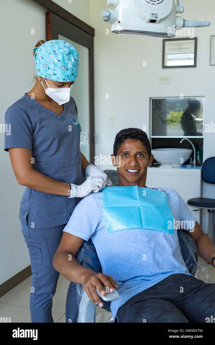 Dentista femminile in studio dentistico che parla con un giovane paziente maschio e si prepara al trattamento. Foto Stock