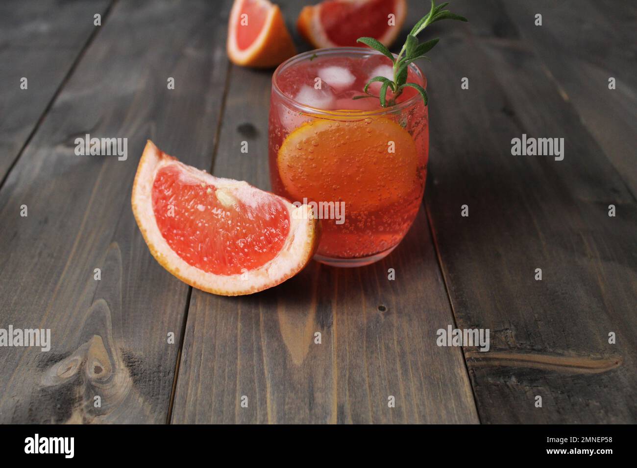 bevi il succo di limonata di pompelmo d'arancia rossa in un bicchiere con una slitta e un rosmarino di menta su uno sfondo grigio con un posto per il testo. Rinfrescare i freddi Foto Stock