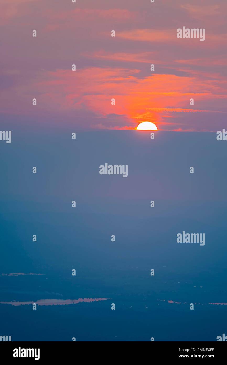 Sole rosso luminoso, tramonto dietro le nuvole all'orizzonte, vista dalla cima di Benediktenwand al tramonto, preAlpi Bavaresi, Baviera, Germania Foto Stock