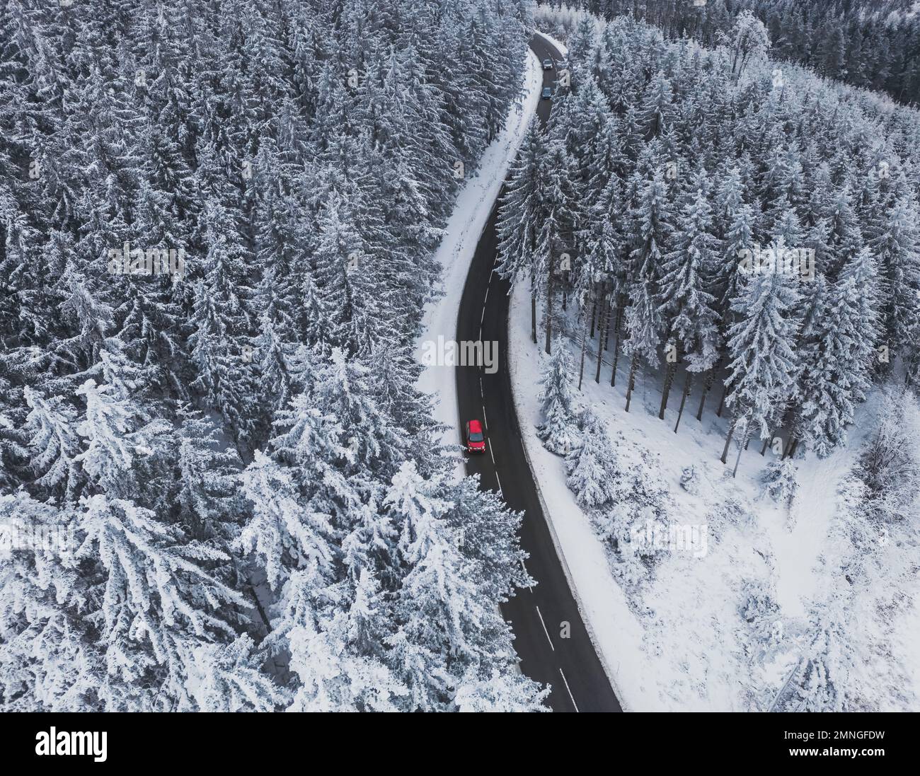 Alberi innevati nella foresta e auto rossa sulla linea stradale in montagna. Paesaggio invernale in montagna. Foto panoramica del drone aereo. Foto Stock