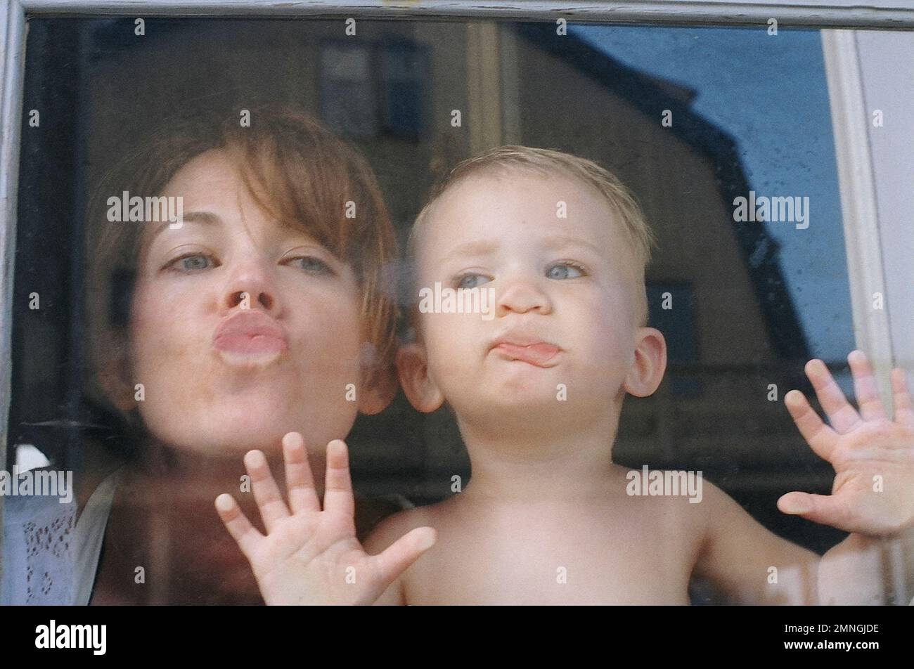 Madre e Figlio giovane premono le labbra contro la finestra in modo chiarito Foto Stock