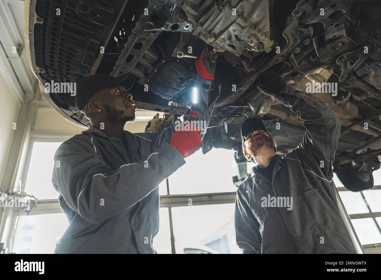 Due meccanici che sostituiscono la frizione di un'auto sollevata utilizzando gli attrezzi di un'officina di riparazione auto. Foto di alta qualità Foto Stock