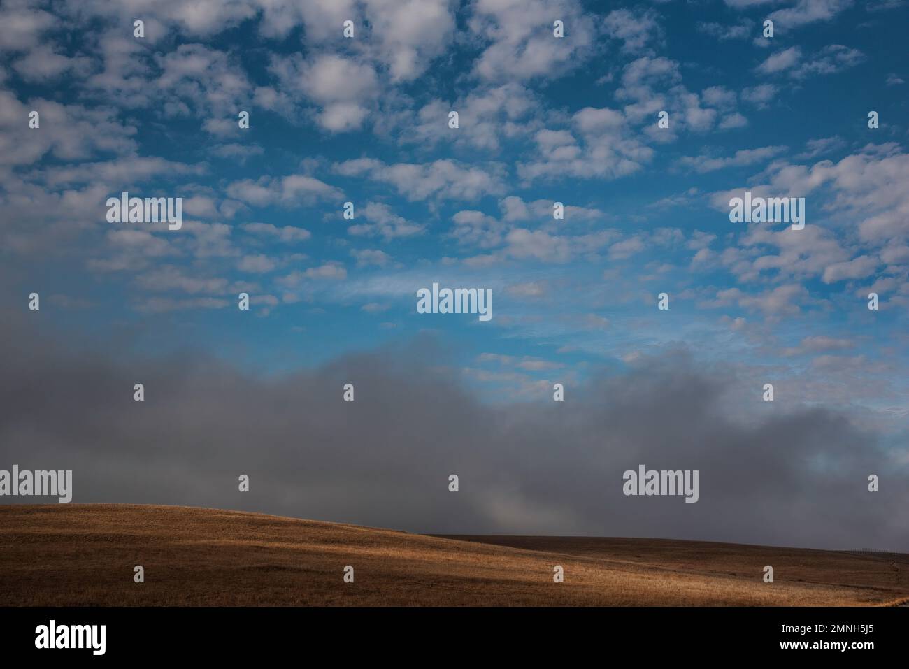 Il raggio del sole attraversa una collina di prateria, il cielo blu punteggiato di nuvole bianche, la riserva naturale delle montagne di Wichita, Oklahoma Foto Stock