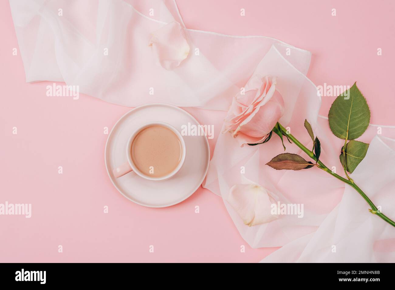 Una tazza da caffè e rosa rosa su tessuto di seta bianca. Concetto di vacanza. Vista dall'alto, disposizione piatta Foto Stock