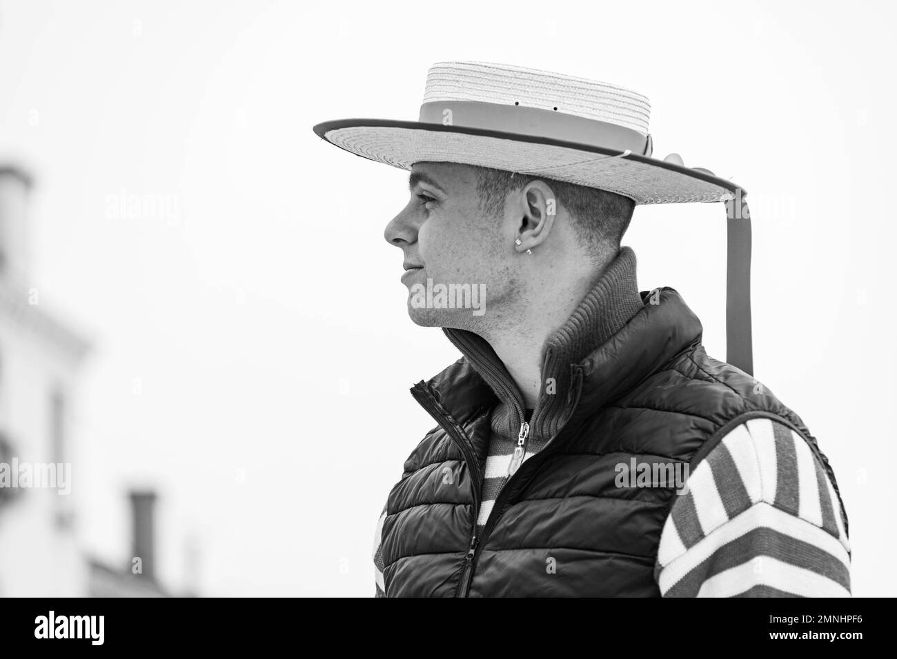 Un gondoliere in un tradizionale cappello di paglia si trova su un ponte di Venezia in attesa di clienti. Le gondole sono un importante mezzo di trasporto turistico a Venezia Foto Stock