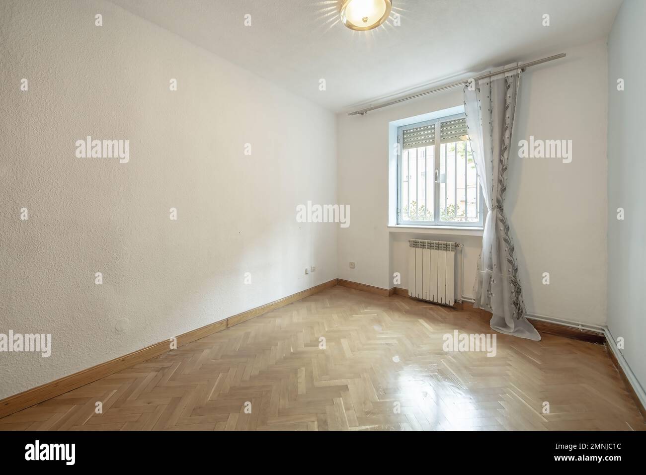 Camera vuota con pavimenti in legno di quercia francese, pareti dipinte in crema, una finestra bianca in alluminio con barre all'esterno e teli tirati. Foto Stock